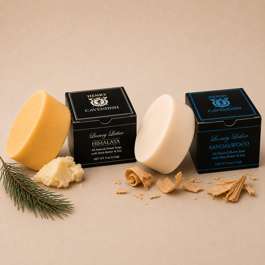 Two bars of Henry Caviship luxury scented soap with their black packaging boxes, styled with natural ingredients on a beige background. One bar is pale yellow with a pine branch and butter piece, and the other is cream-colored with sandalwood shavings.