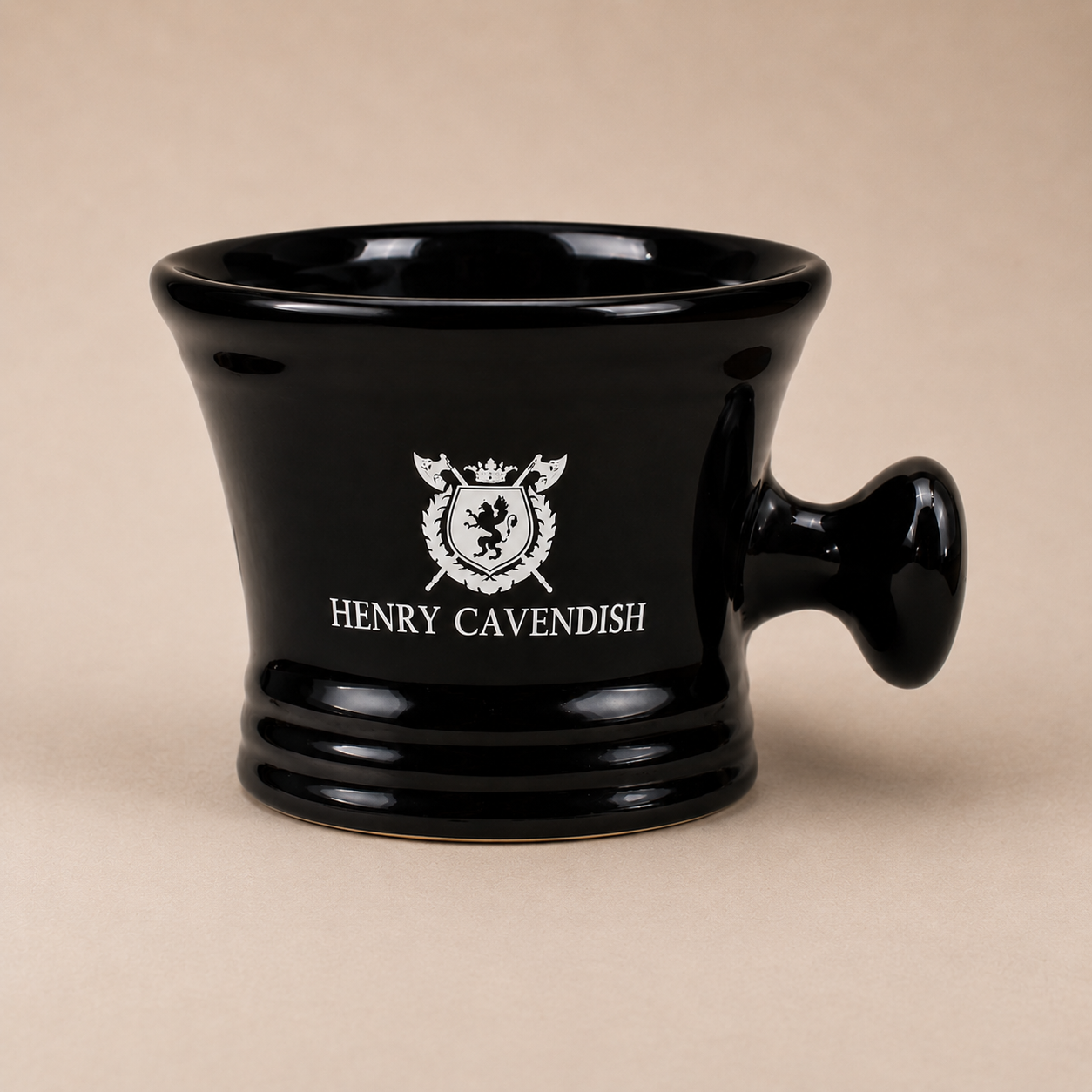 A glossy black ceramic mortar and pestle with a handle, featuring a white printed crest and the text 'HENRY CAVENDISH' on the front, set against a solid beige background.