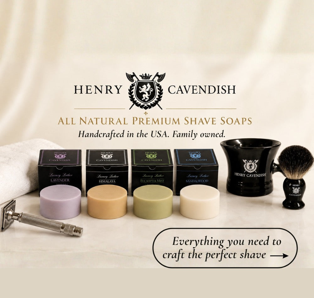 Henry Cavendish All Natural Premium Shave Soaps set displayed on a draped cream fabric background, featuring four boxed soaps, four round soap bars in pastel colors, a black shaving bowl, a shaving brush, a metal safety razor, and branded packaging with the Henry Cavendish logo.