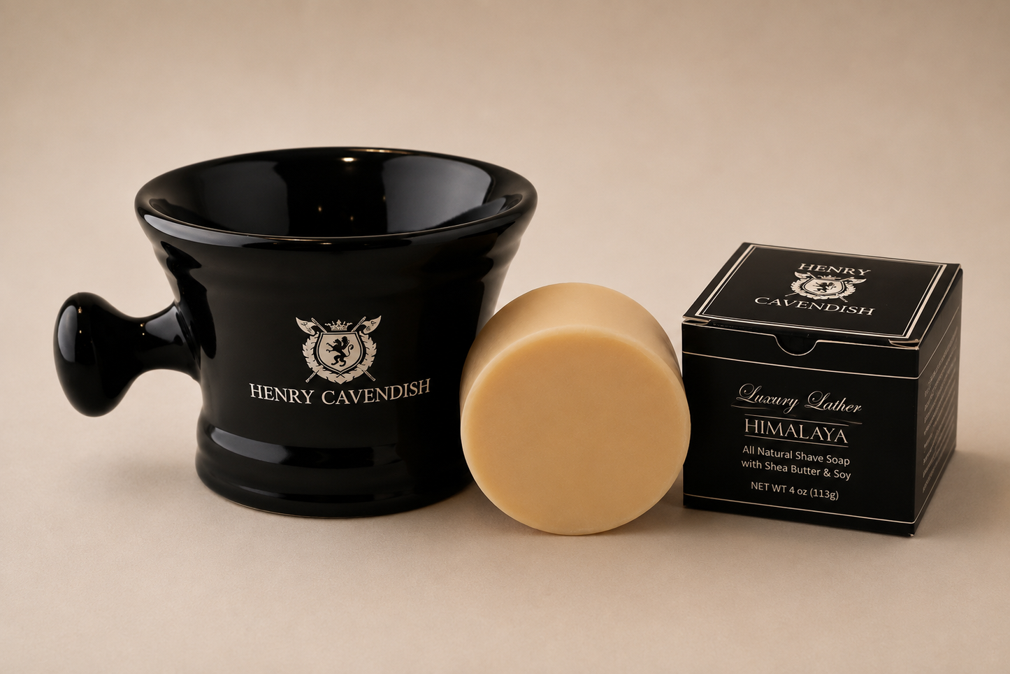 Henry Cavendish Himalaya luxury shave soap set, featuring a black ceramic shaving bowl with the brand logo, a round pale beige soap bar, and its black retail box on a neutral beige background.